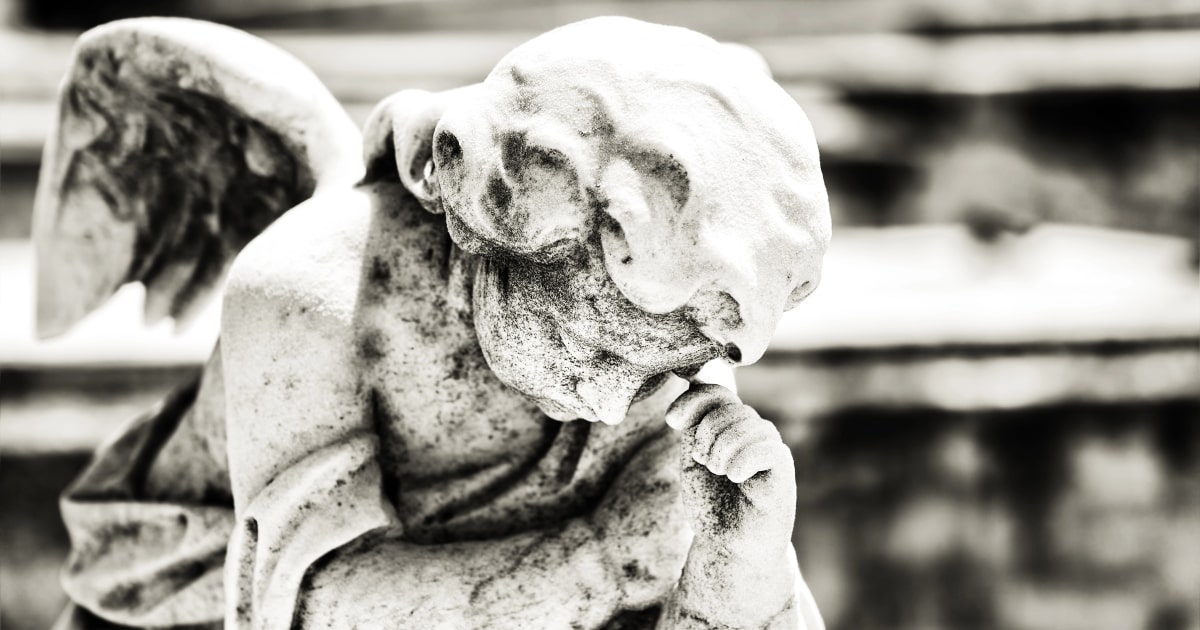 Stone angel statue in a cemetery, bowing its head in mourning.