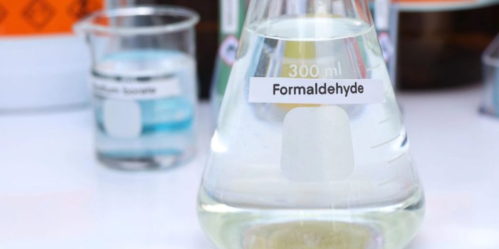 Clear laboratory flask labeled formaldehyde on a white bench for a blog explaining what is formaldehyde.