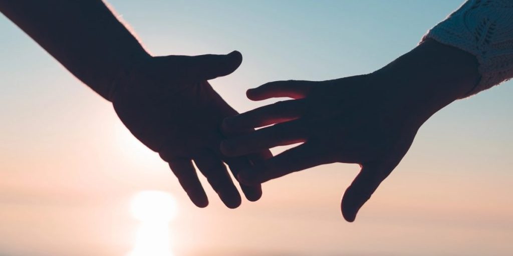Two hands reaching toward each other at sunset, symbolising compassion and connection in how to support someone who is grieving.